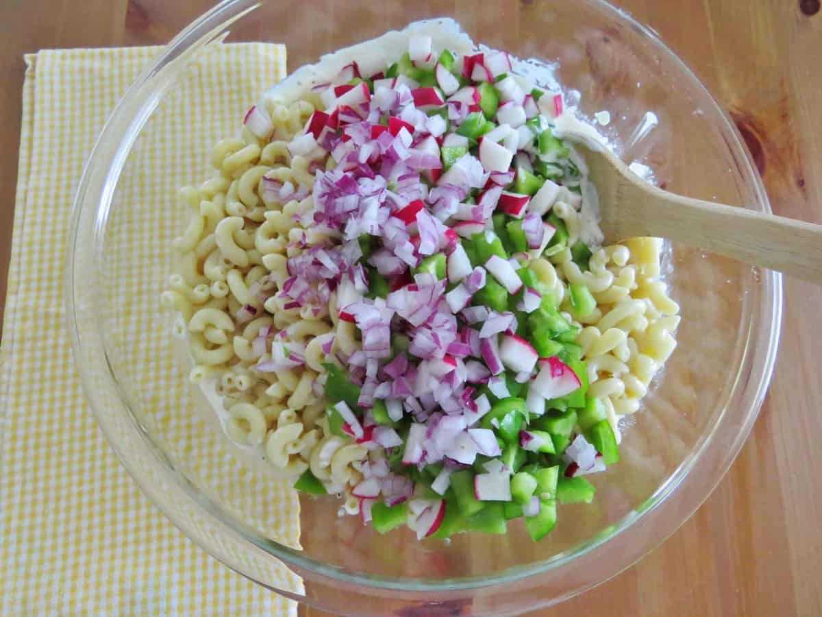 cooked macaroni noodles, green peppers, radishes, diced onions and cream mixture in a bowl.