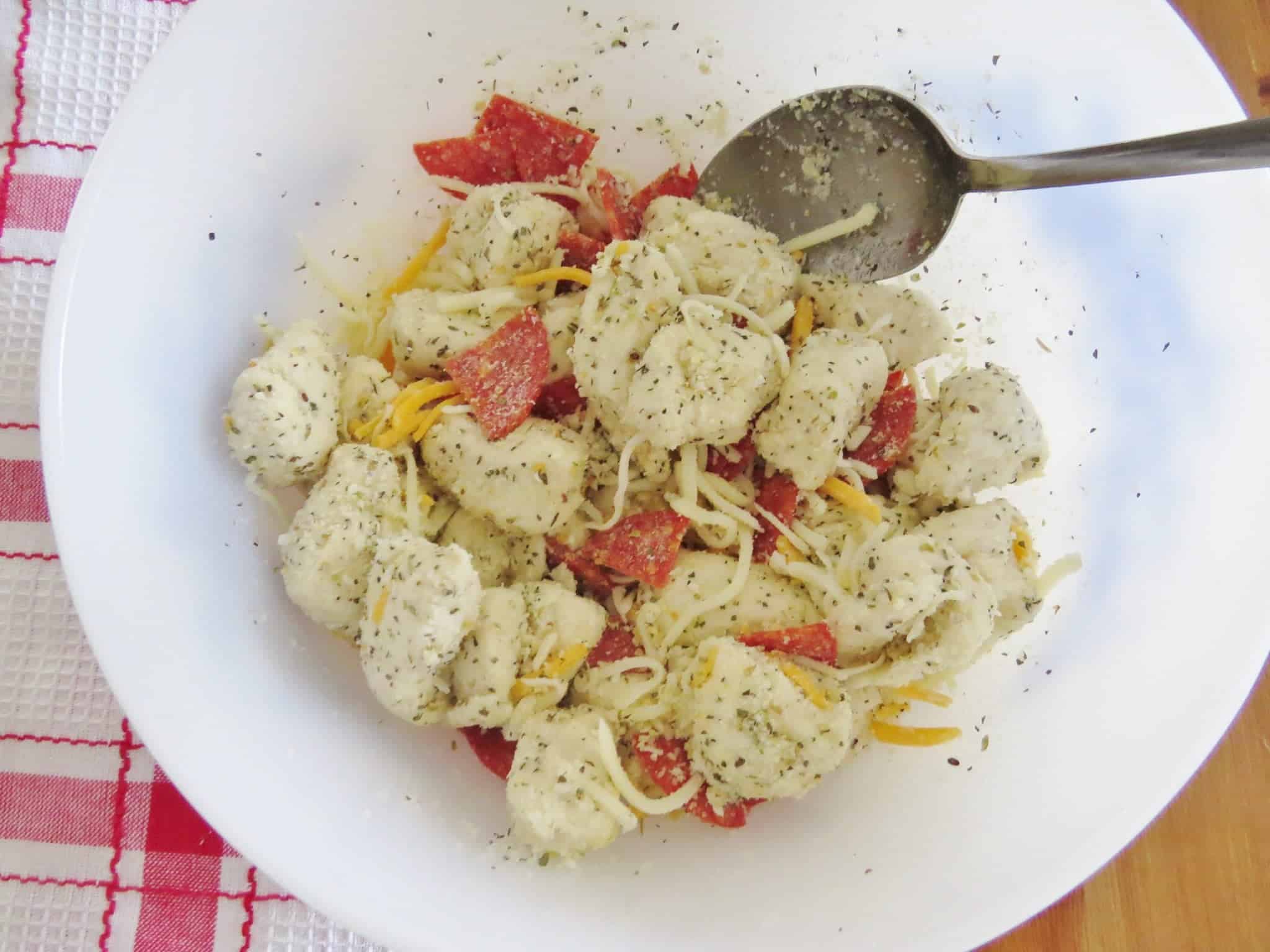 biscuits tossed with cheese, Italian seasoning, onion powder, garlic salt, sliced pepperoni tossed in a bowl.