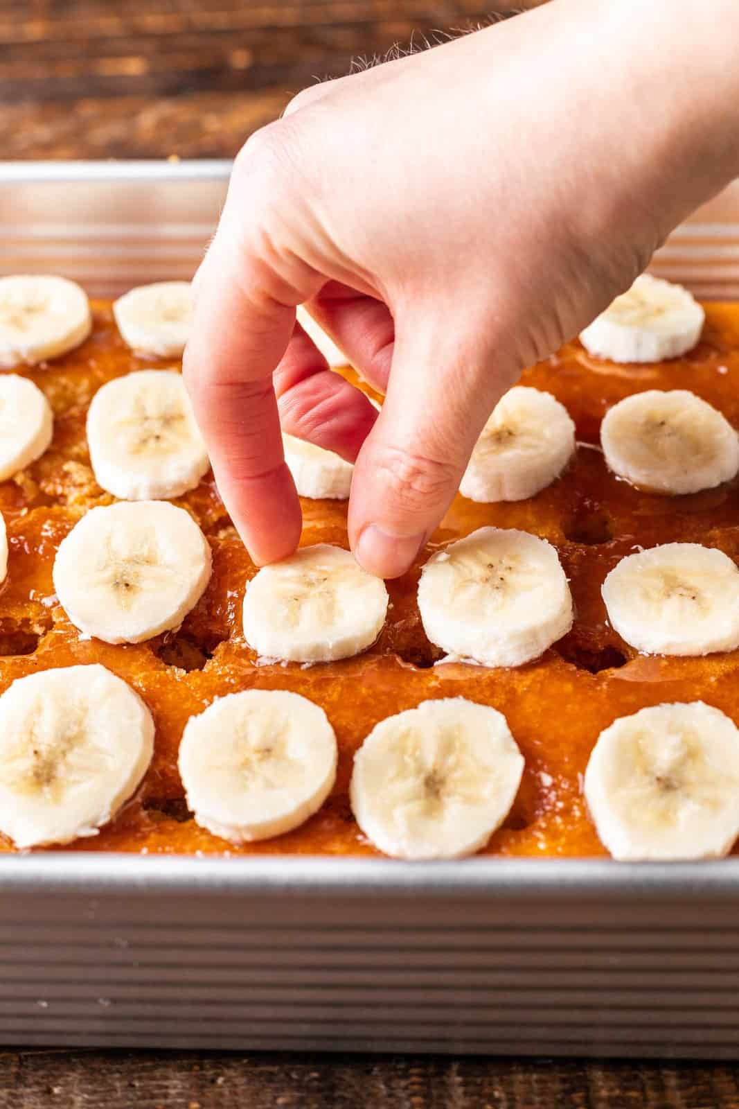 a hand placing sliced bananas evenly on top of cake. 