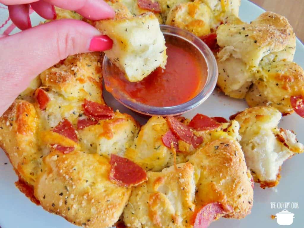 hand shown ipping pizza biscuits in pizza sauce.