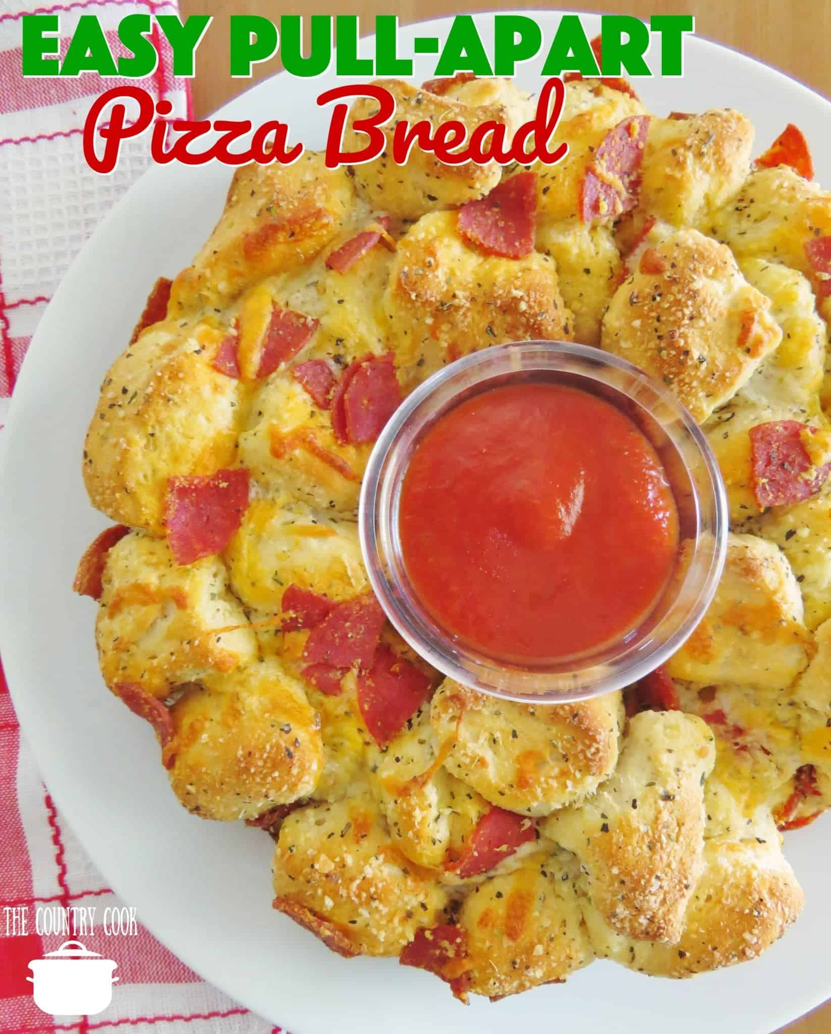 Easy Pizza Pull Apart Pizza Bread recipe from The Country Cook. Pull apart bread shown on a round white plate with a bowl of marinara sauce in the middle. 