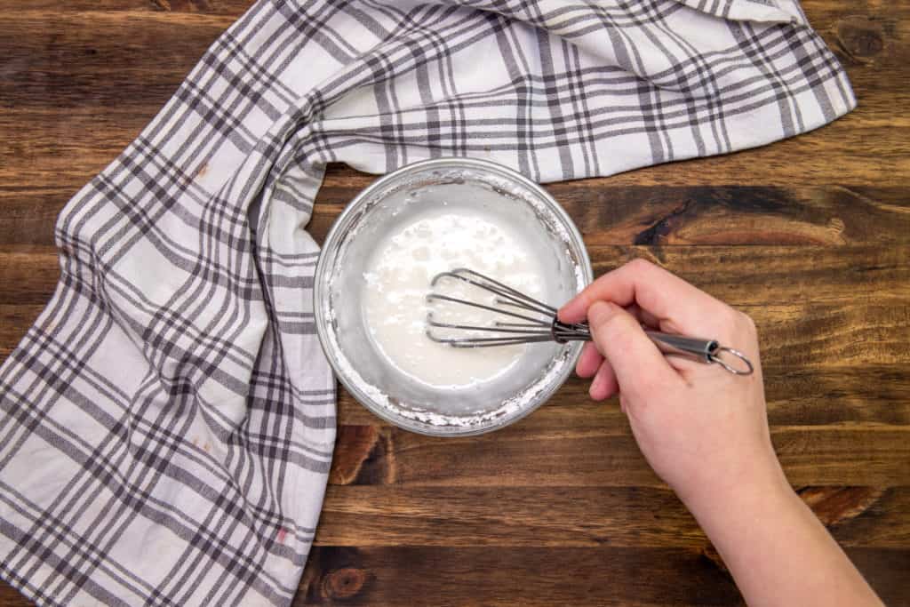 whisking together milk and powdered sugar in a bowl.