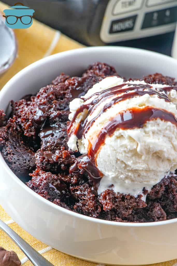 Slow Cooker Chocolate Fudge Cake shown served in a white bowl topped with a scoop of vanilla ice cream and drizzled with chocolate sauce