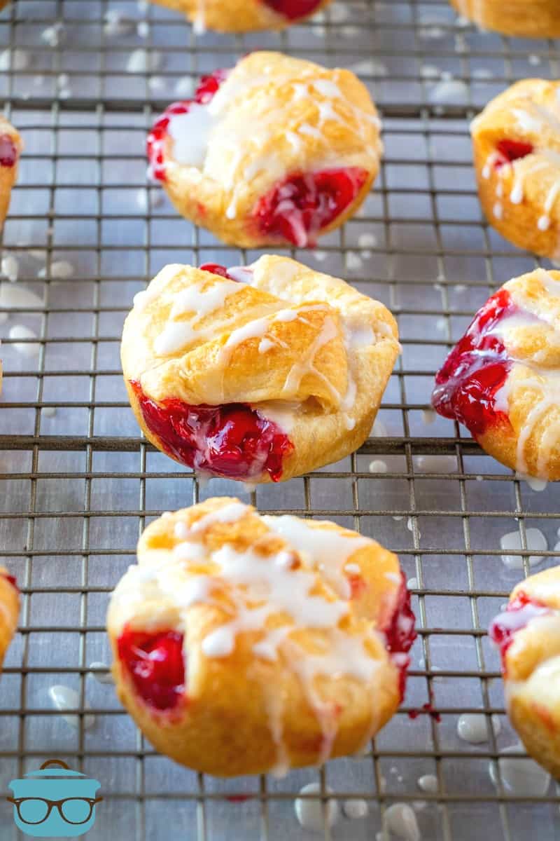 icing drizzled on top of cherry pie bites on a cooling rack.