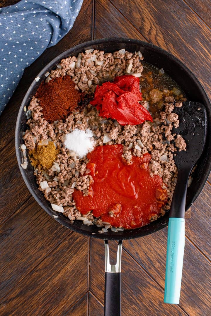 seasonings, tomato sauce and tomato paste added to cooked ground beef in a skillet. 