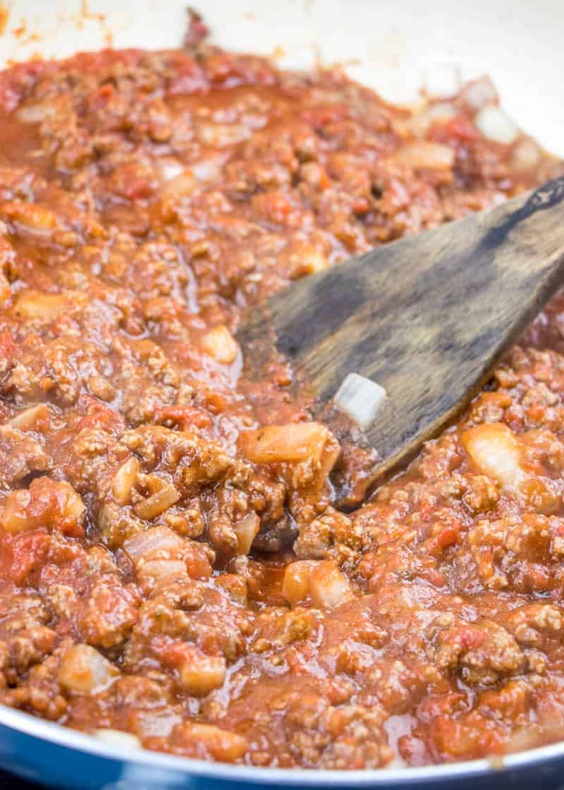 crushed tomatoes, tomato sauce added to ground beef in a skillet with a wooden spatula. 