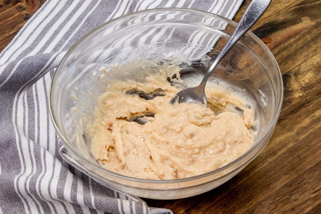metled butter and apple cinnamon muffin mix combined together in a clear mixing bowl with a spoon
