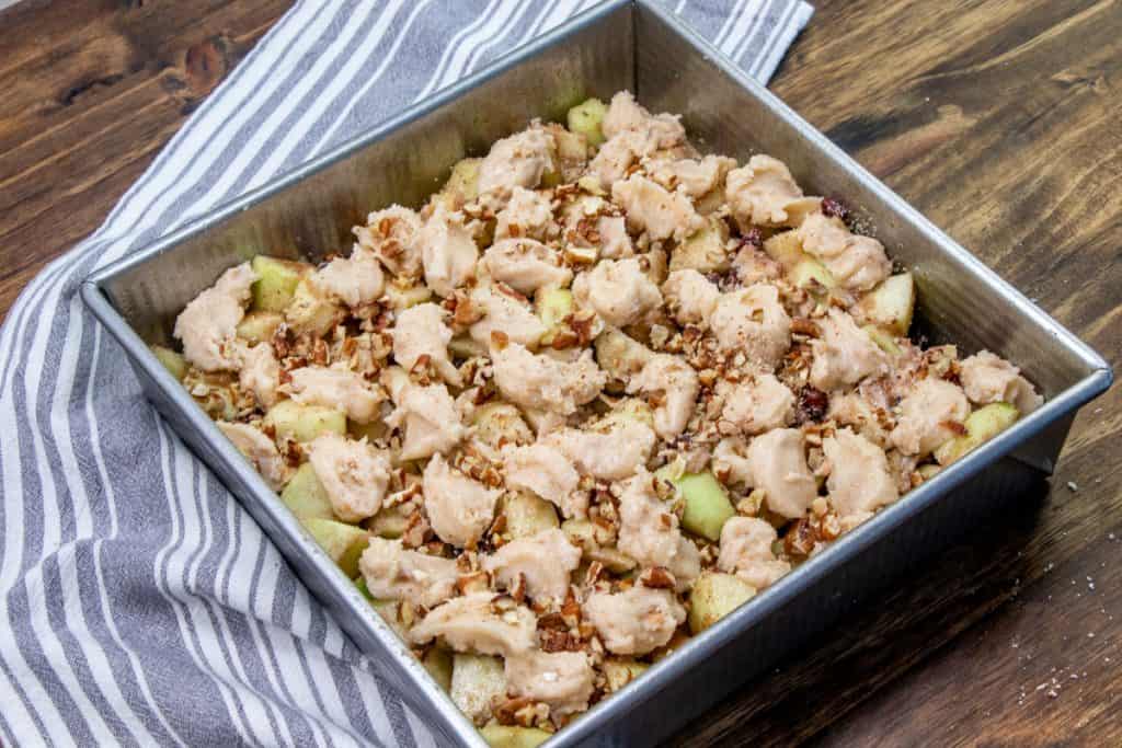 apple cinnamon cobbler topping dropped by the spoonful and chopped pecans on top of chopped apples in a baking dish