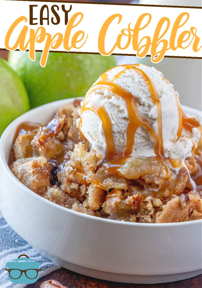 Easy apple cobbler recipe from The Country Cook, shown served in a white serving bowl and topped with a coop of vanilla ice cream drizzled with caramel and two green apples in the background.
