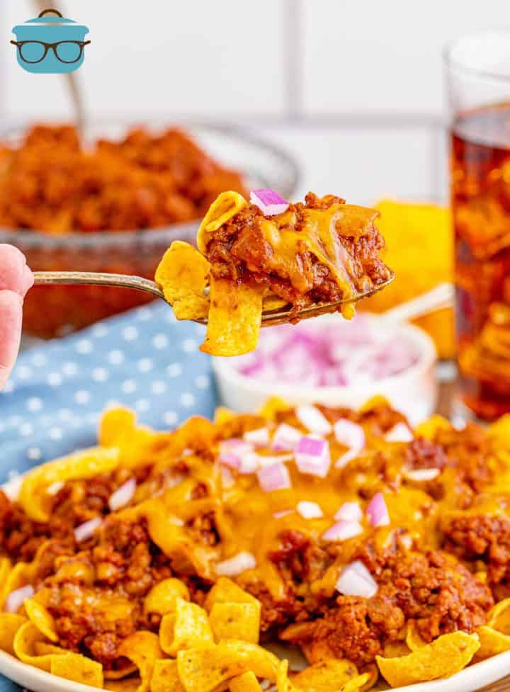a fork holding up a serving of Frito Chili Pie with a glass of iced tea in the background.
