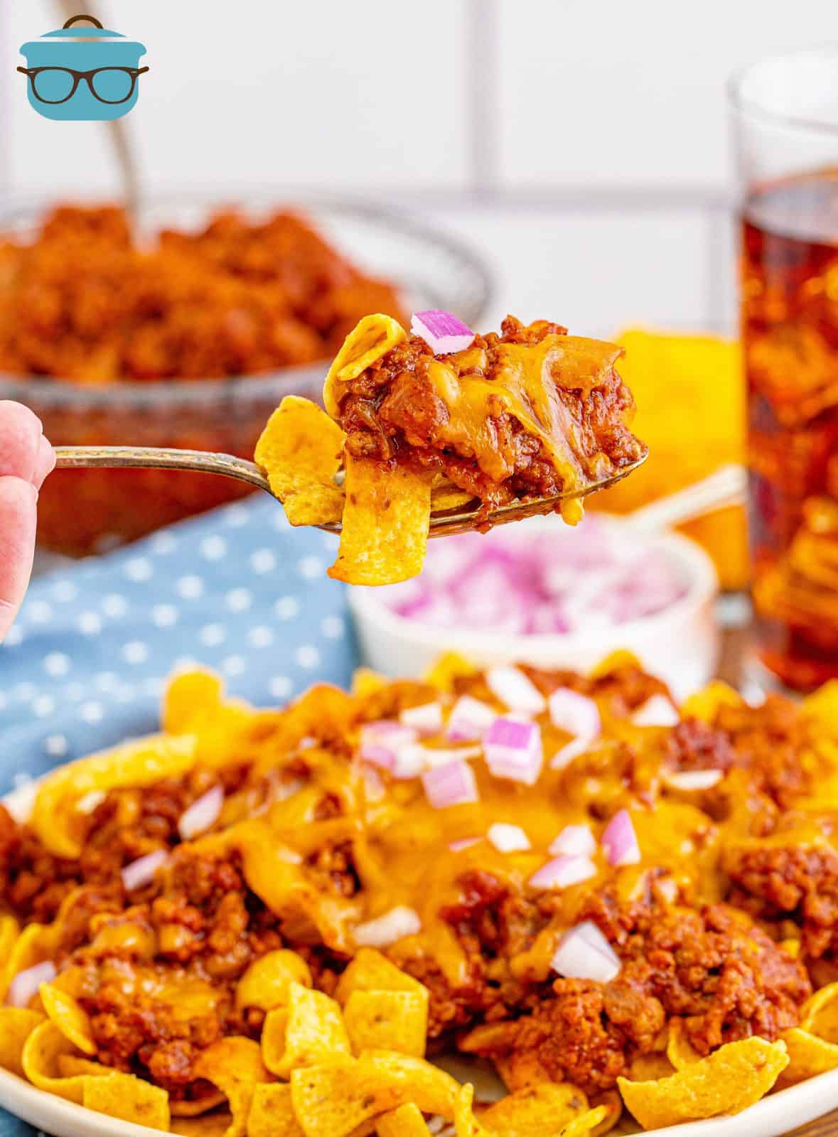 a fork holding up a serving of Frito Chili Pie with a glass of iced tea in the background.