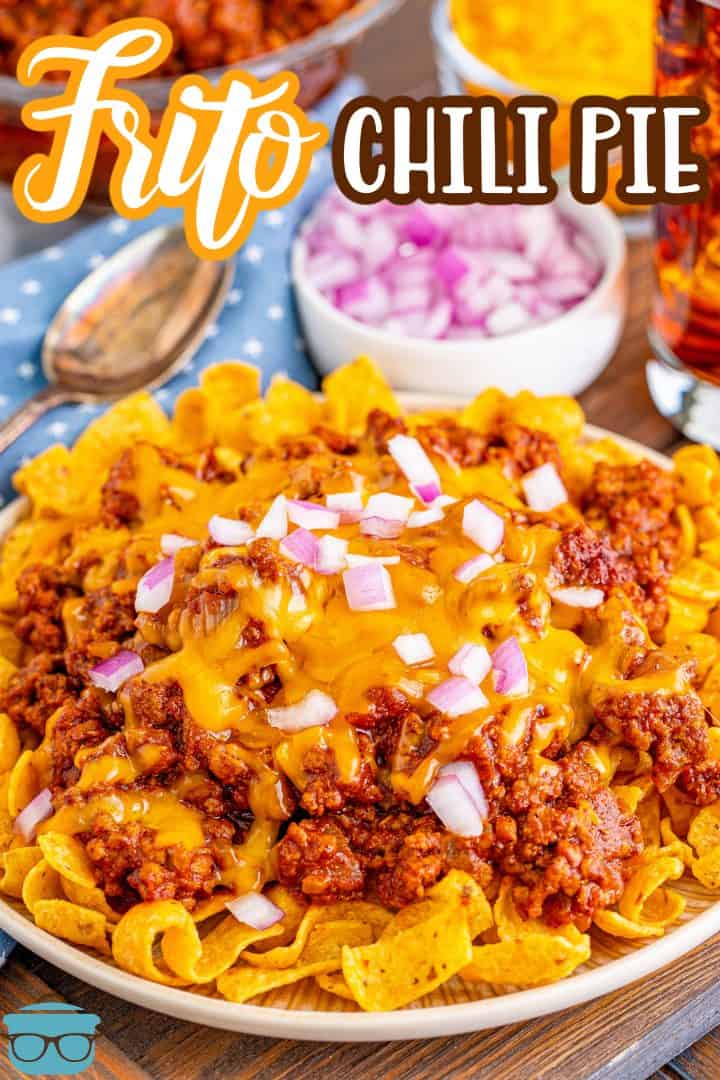 A small round white plate topped with Frito corn chips and topped with chili with melted cheese and diced onion.