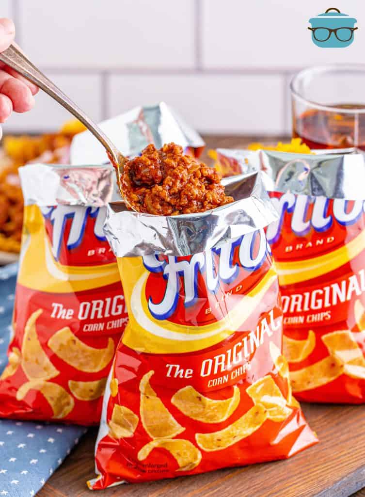 spoon pouring chili into a bag of Fritos corn chips.