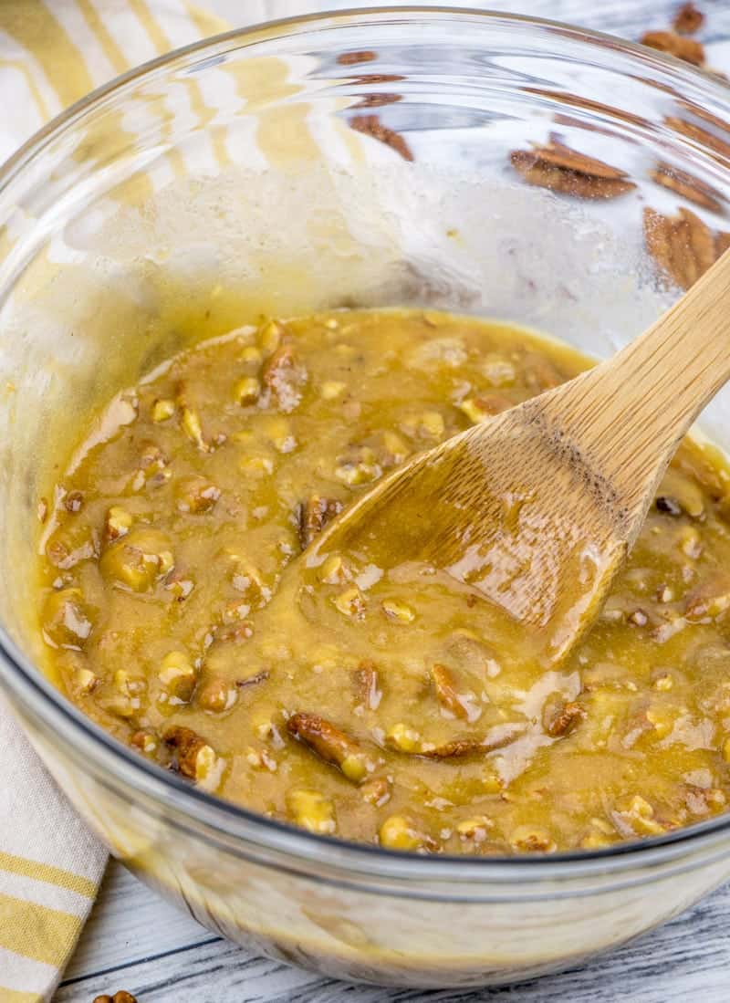 pecan pie muffin batter in a clear bowl being stirred with a wooden spoon.