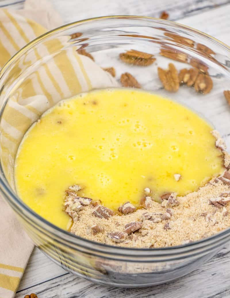 egg and melted butter being mixed with flour, brown sugar and chopped pecans in a bowl.