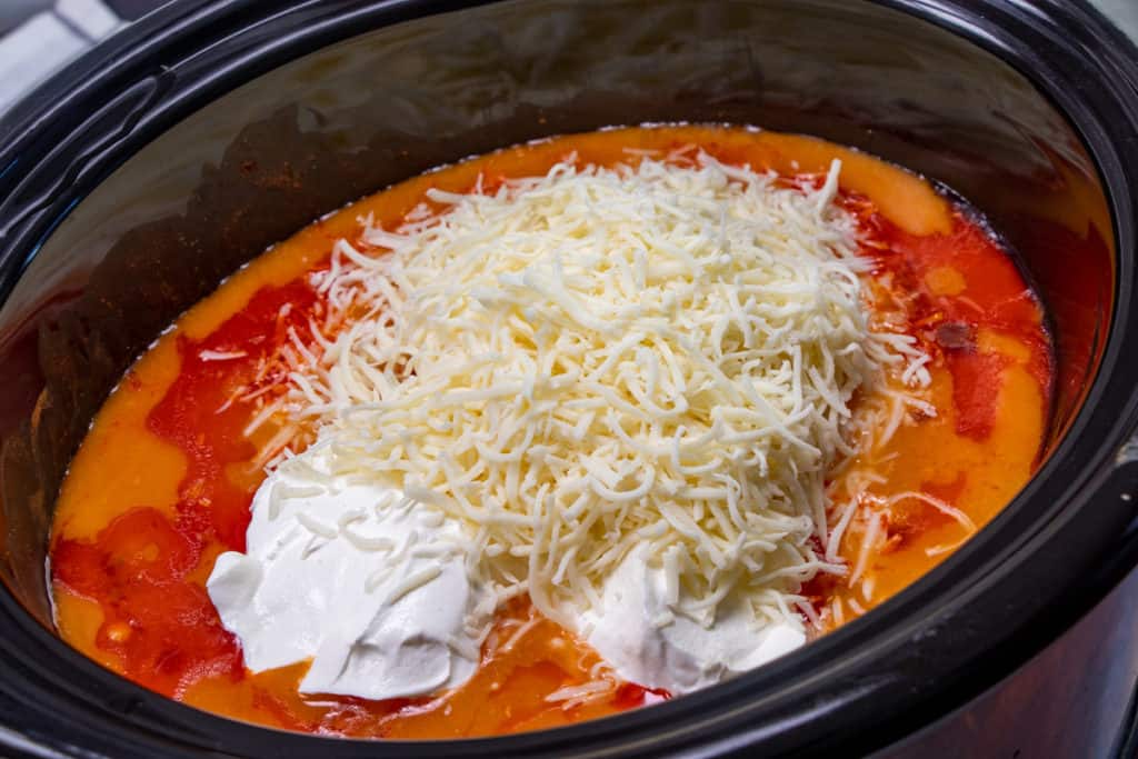 shredded mozzarella and sour cream on top of cooked buffalo chicken mixture in slow cooker