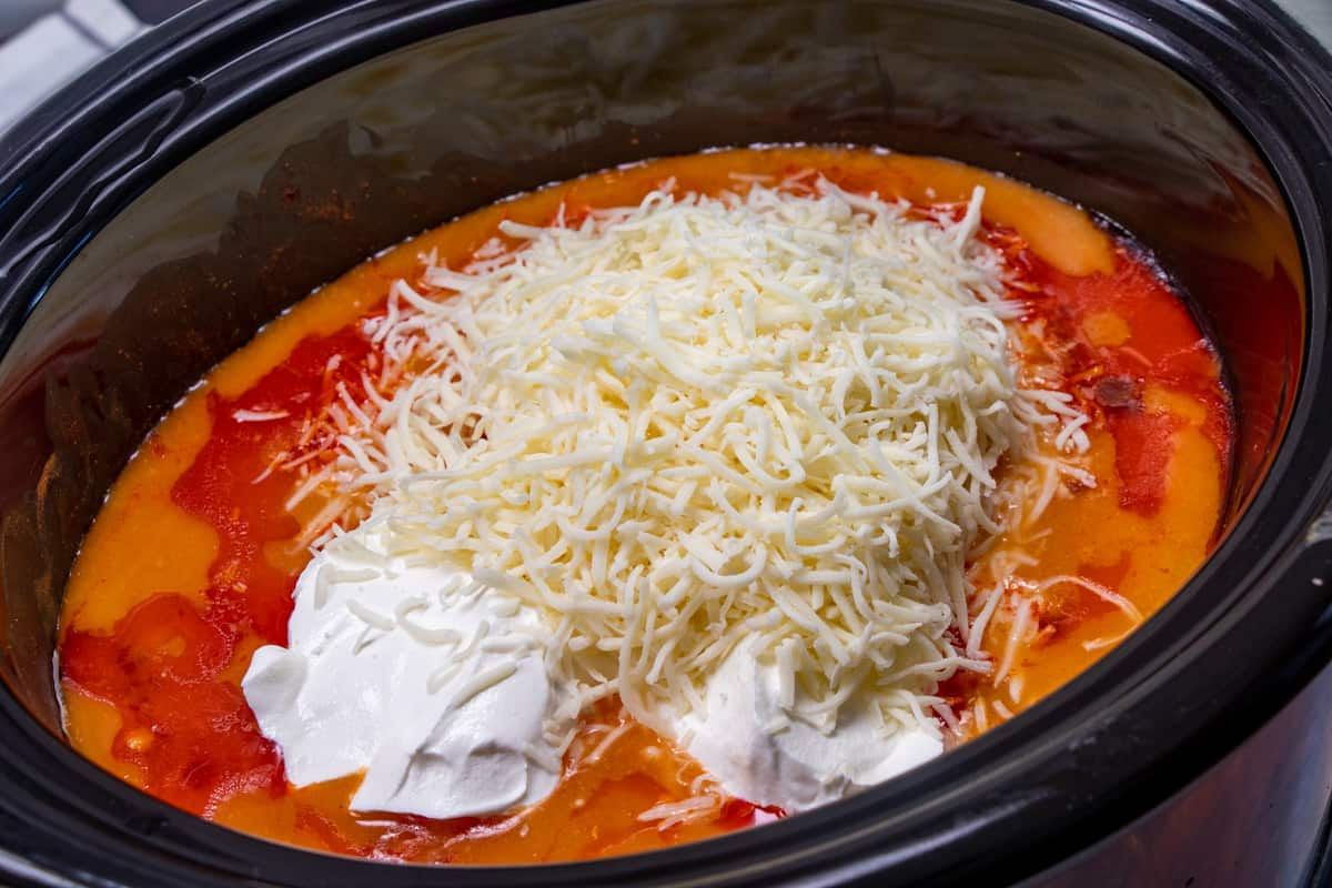 shredded mozzarella and sour cream on top of cooked buffalo chicken mixture in slow cooker.