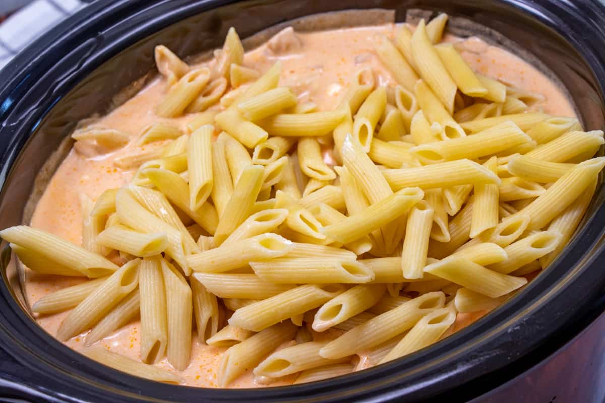 cooked penne pasta added to the top of buffalo chicken and cheese mixture in the slow cooker.