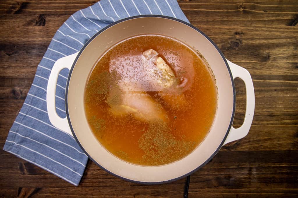 chicken added to chicken broth and seasonings in a large stock pot