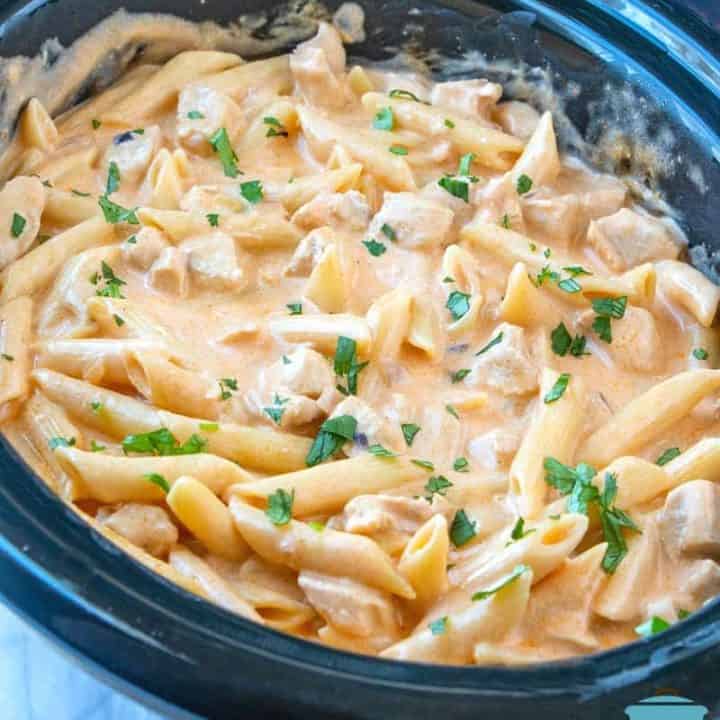 Crock Pot Buffalo Chicken Pasta, fully cooked in an oval slow cooker, topped with chopped parsley