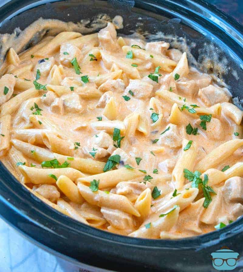 Crock Pot Buffalo Chicken Pasta, fully cooked in an oval slow cooker, topped with chopped parsley.