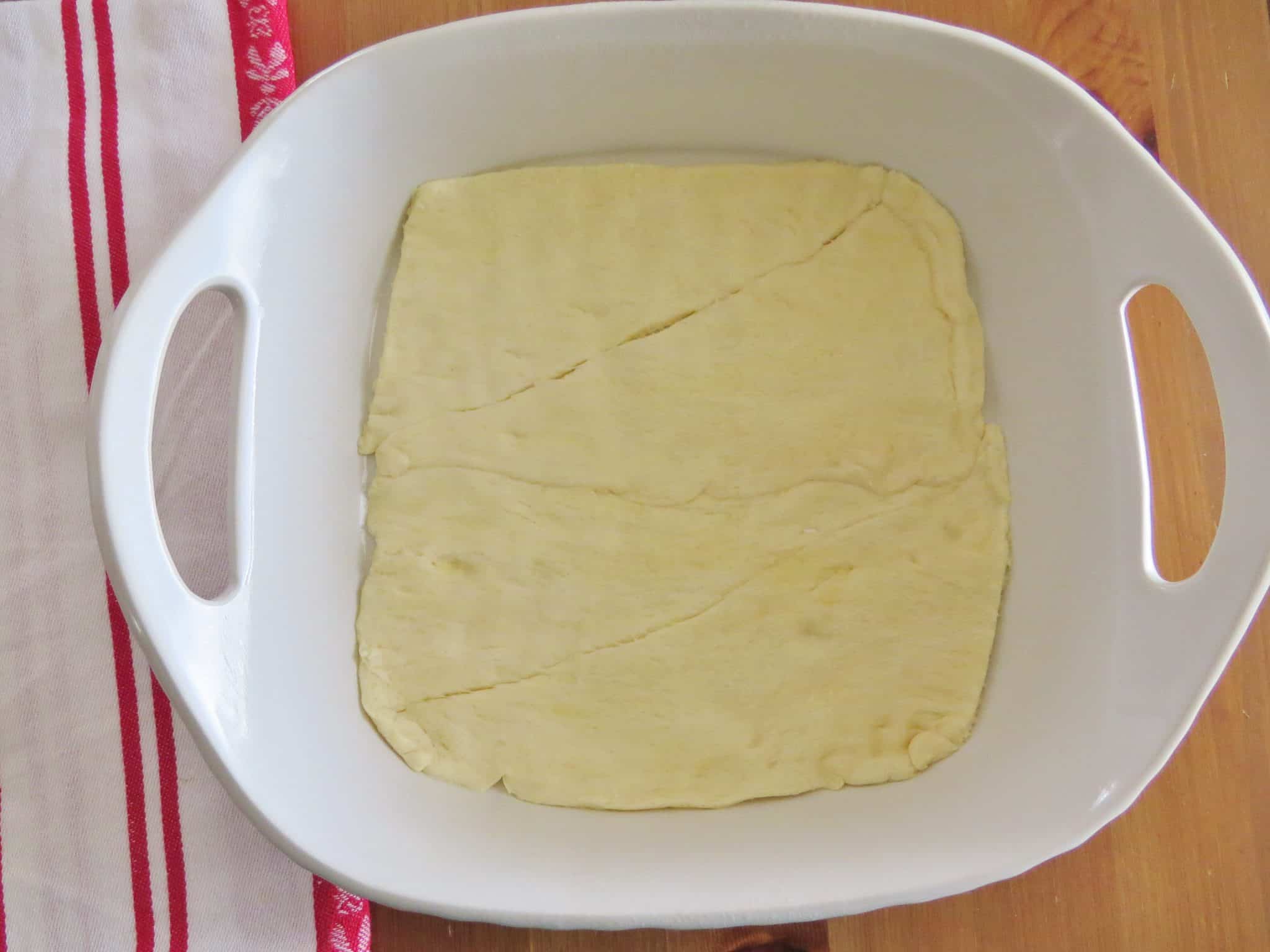 crescent roll dough spread into the bottom of a white baking dish.