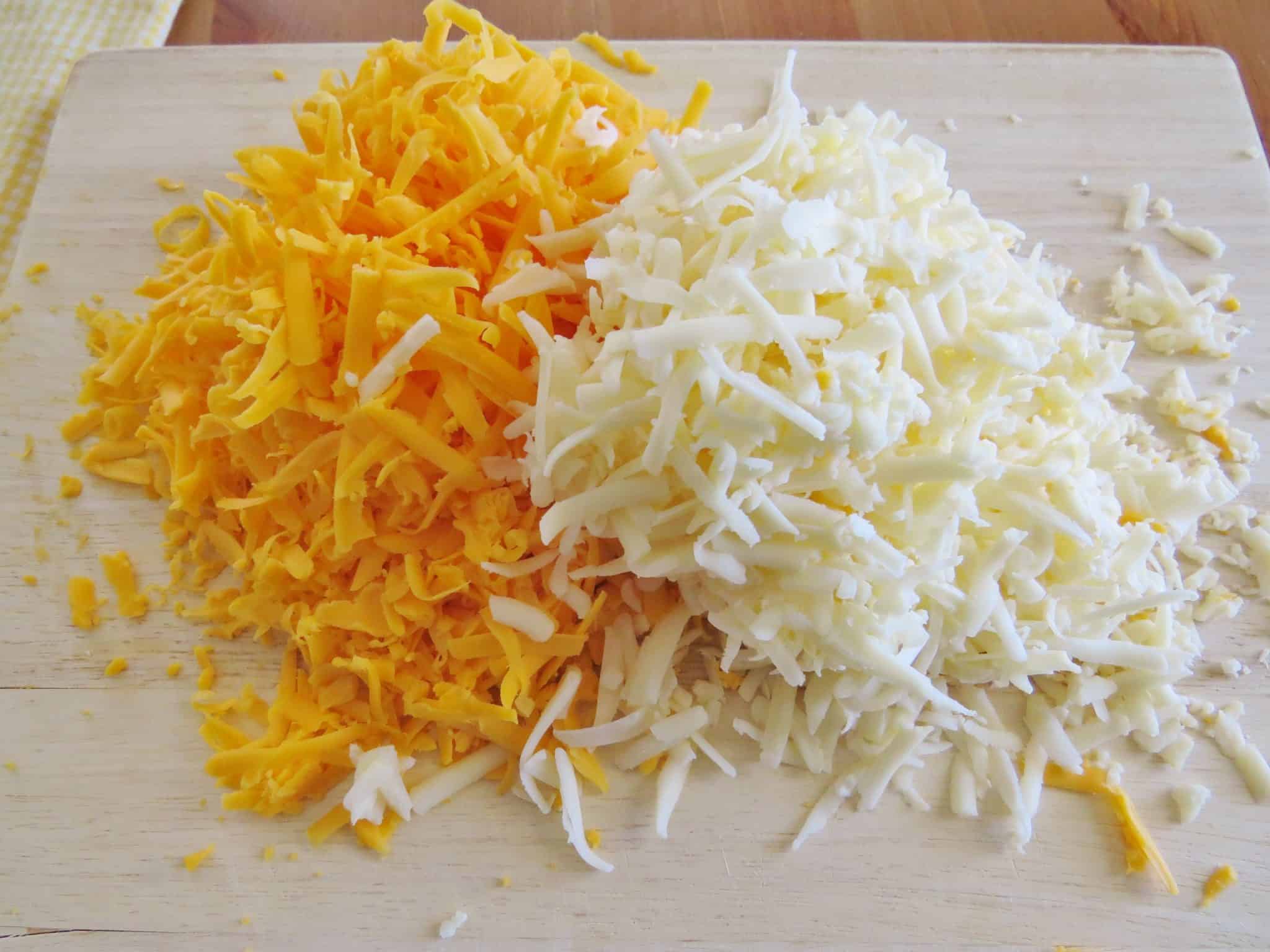 shredded cheddar and Monterey Jack cheeses on a cutting board.