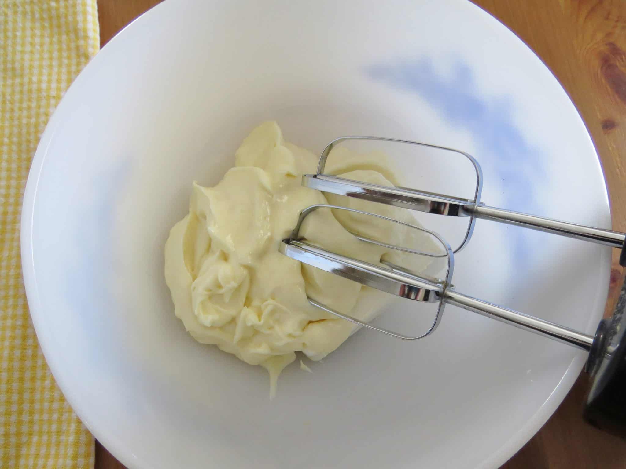cream cheese and mayonnaise mixed together with an electric mixer in a white bowl.