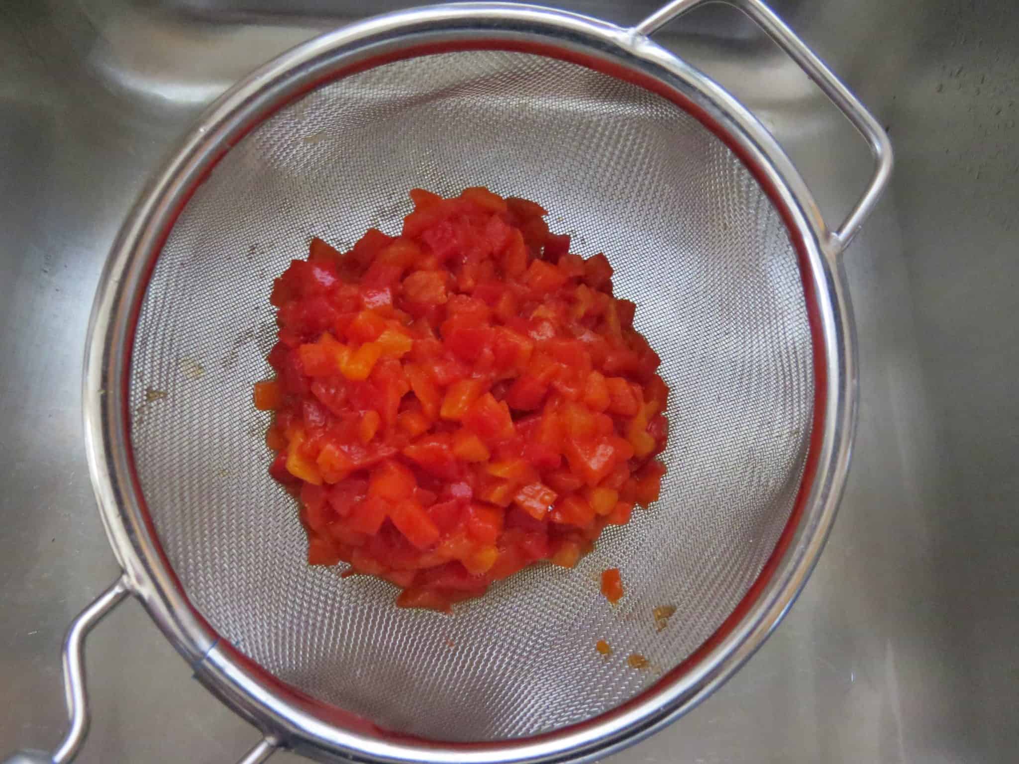 draining jar of diced pimientos in a metal mesh strainer.