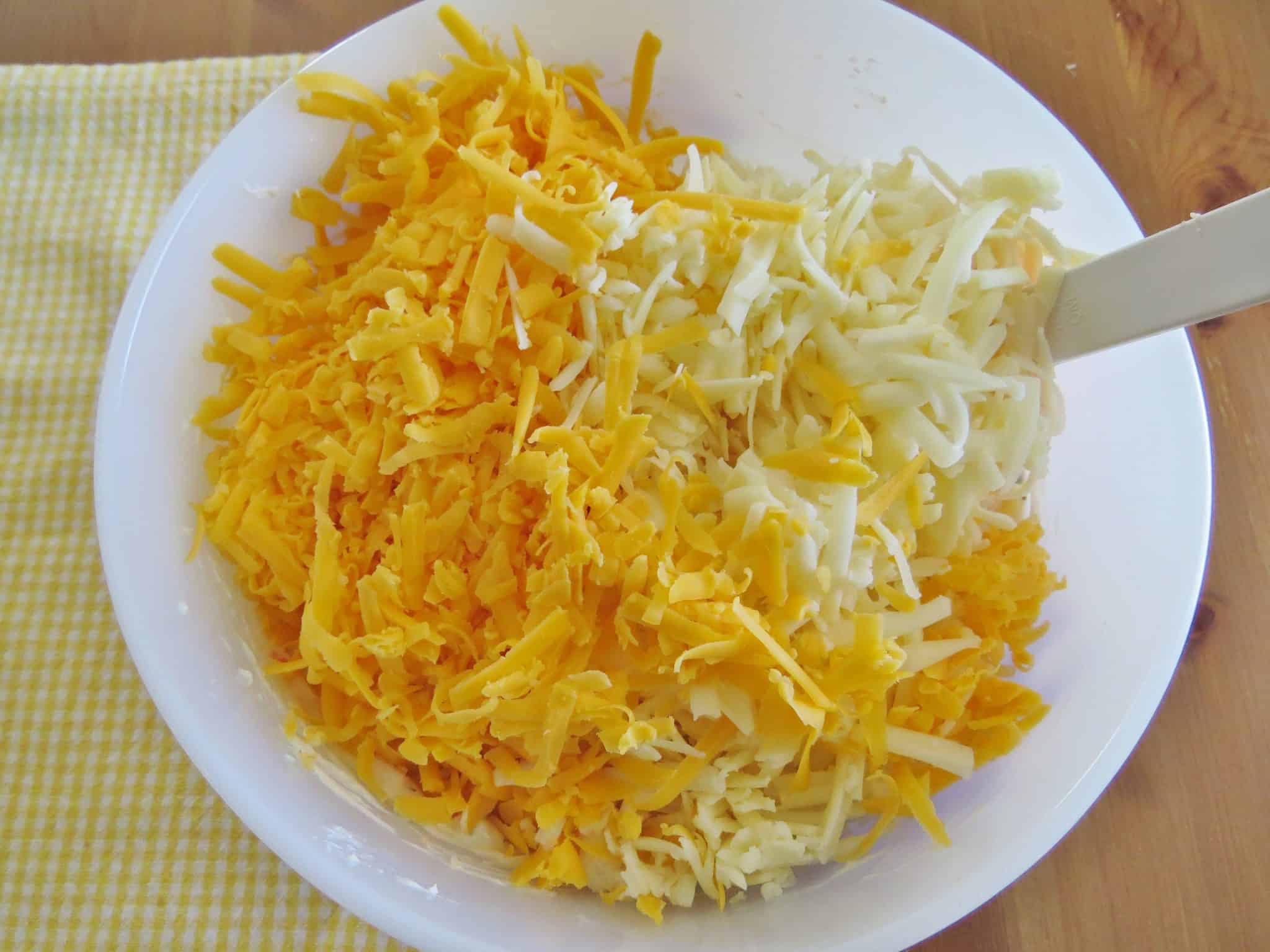 shredded cheddar cheeses added to seasoned cream cheese mixture in a large bowl.