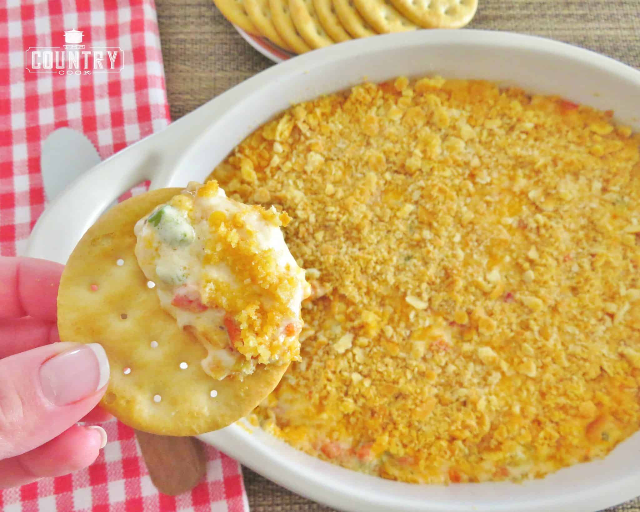 a hand holding up a butter crack topped with warm pimento cheese dip.