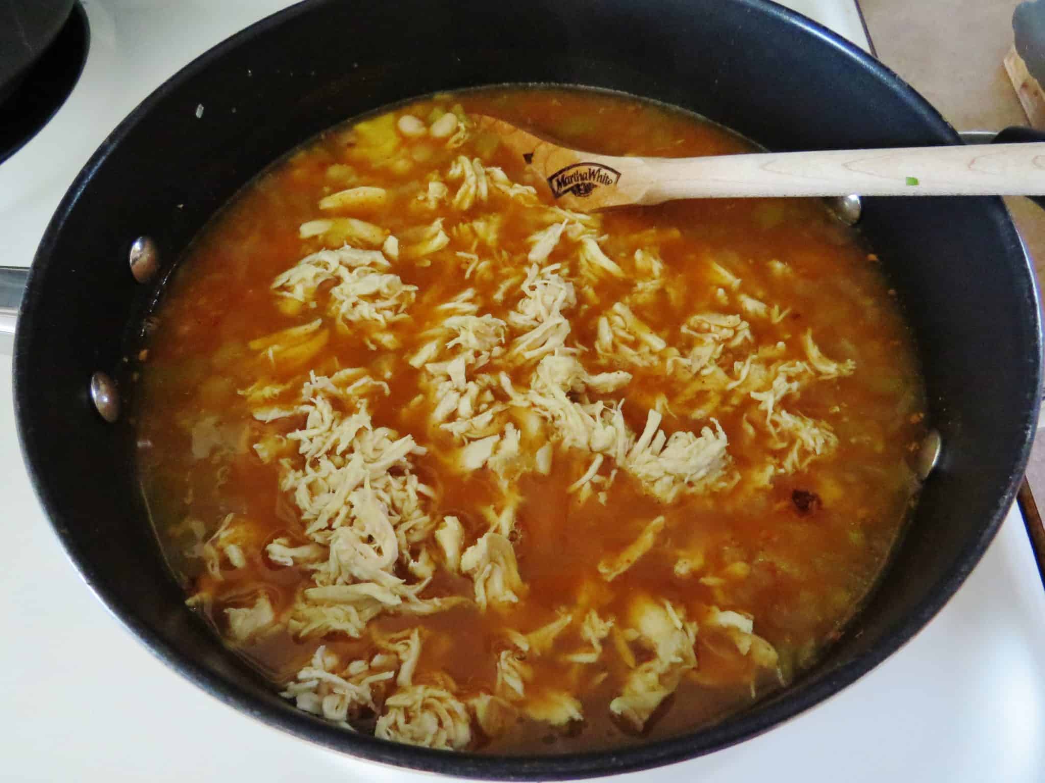 shredded chicken and chicken broth shown in a pot with a wooden spoon.