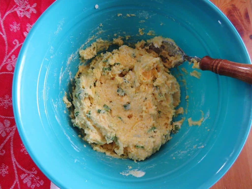 cornbread batter, green onion, eggs, cheese stirred together in a blue bowl 