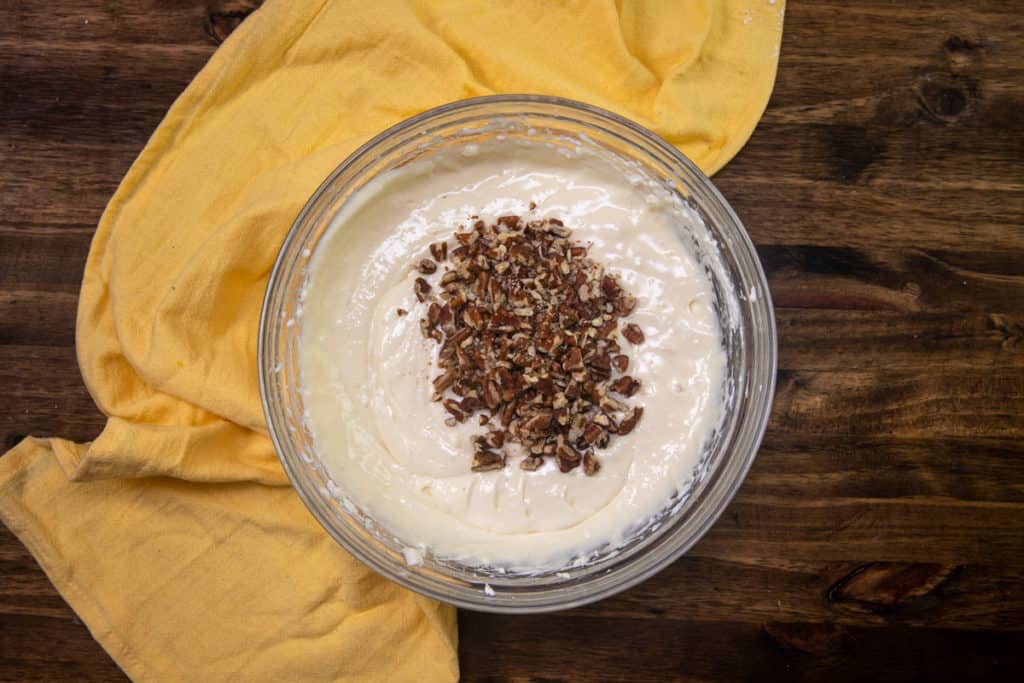 chopped pecans added to cheesecake batter in large clear bowl
