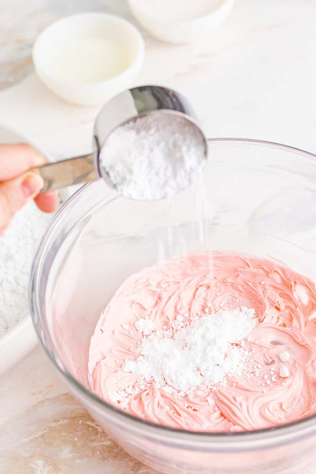 powdered sugar being added to cream cheese and food coloring mixture.