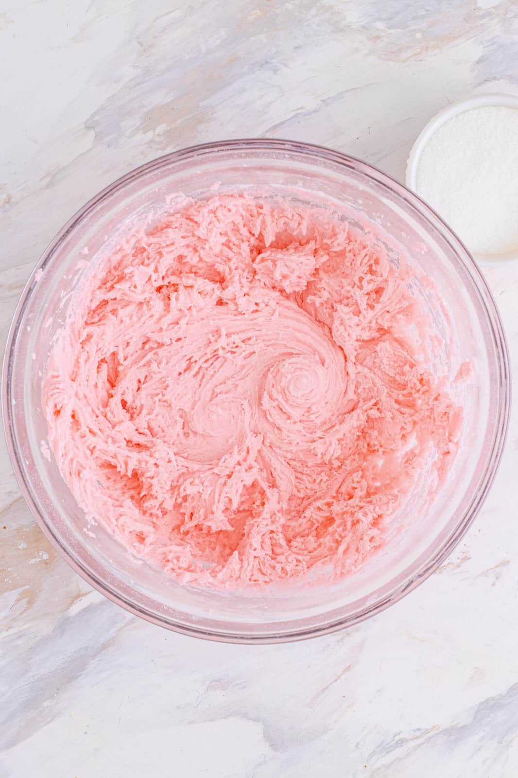 cream cheese and red food coloring mixed together in a clear bowl.