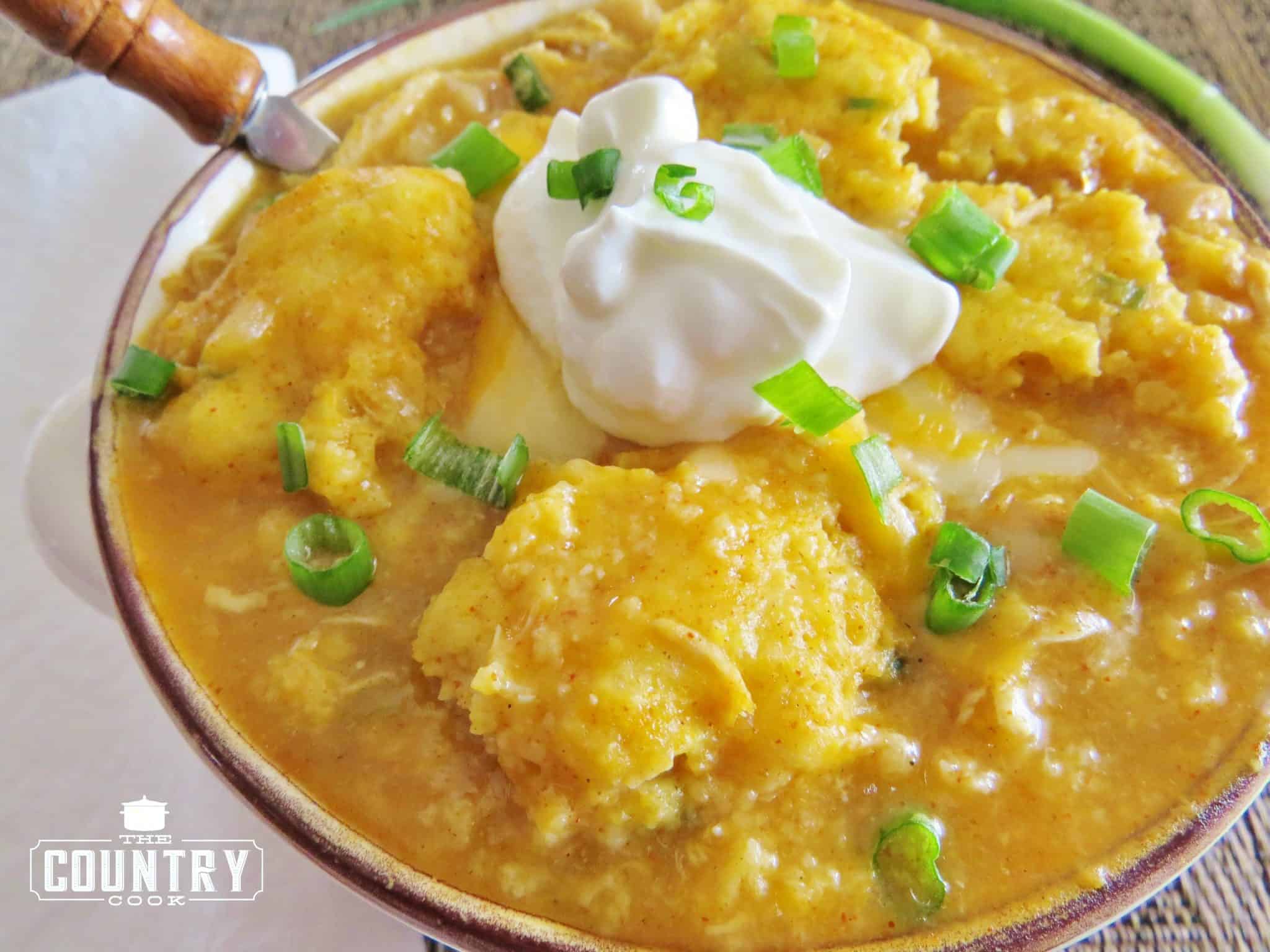 White Chicken Chili with Cornbread Dumplings shown in a bowl with a dollop of sour cream on top with sliced green onions.