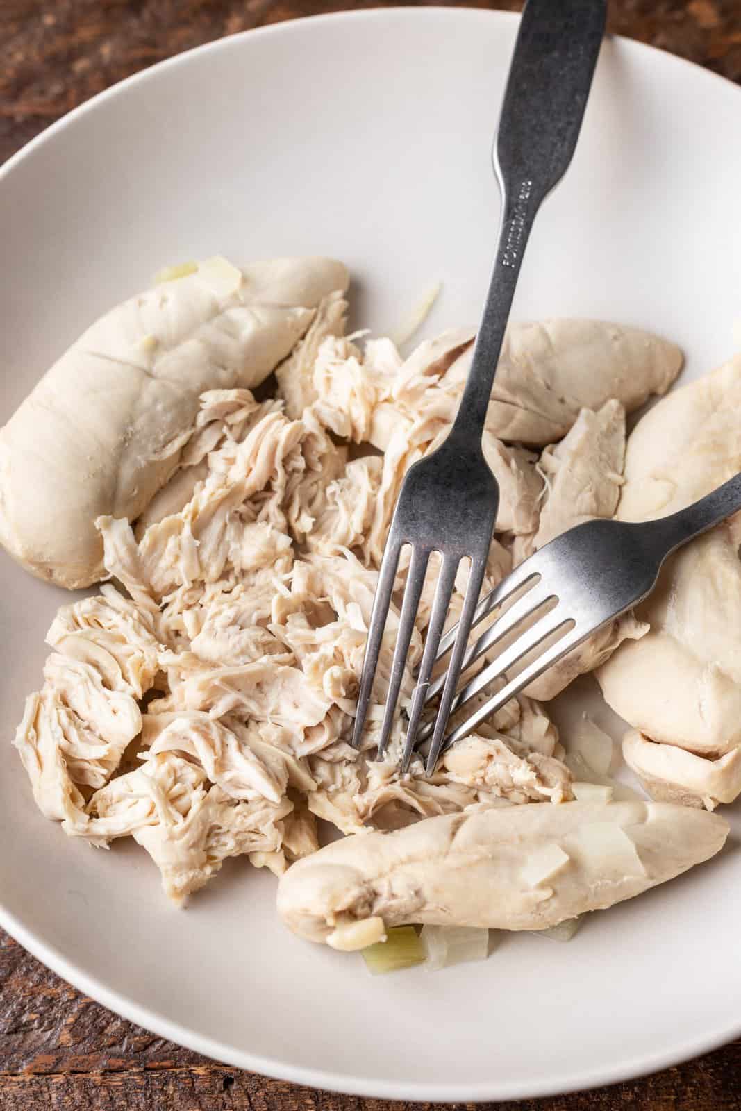 shredding chicken with two forks in a bowl.