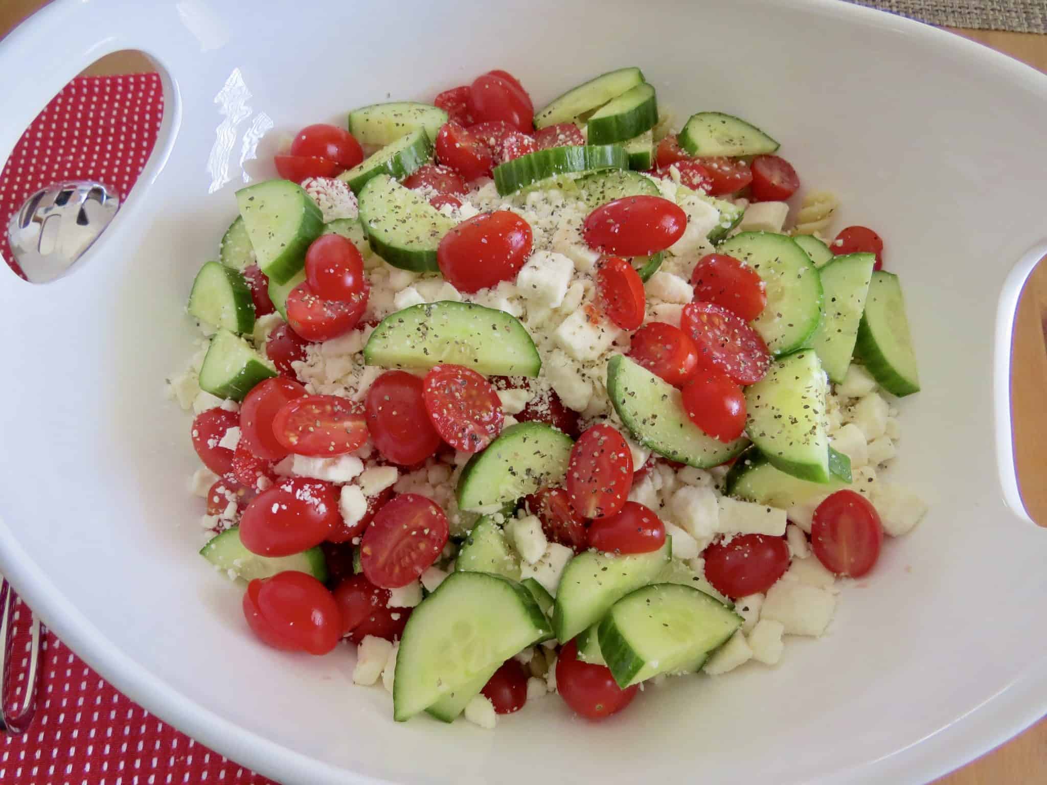 tomatoes, cucumbers, feta cheese and rotini pasta in a large white serving bowl.