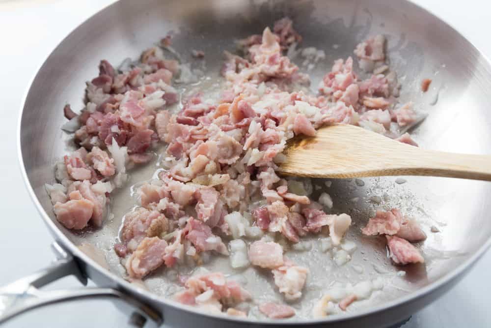 saute onion and bacon in a skillet with a wooden spoon