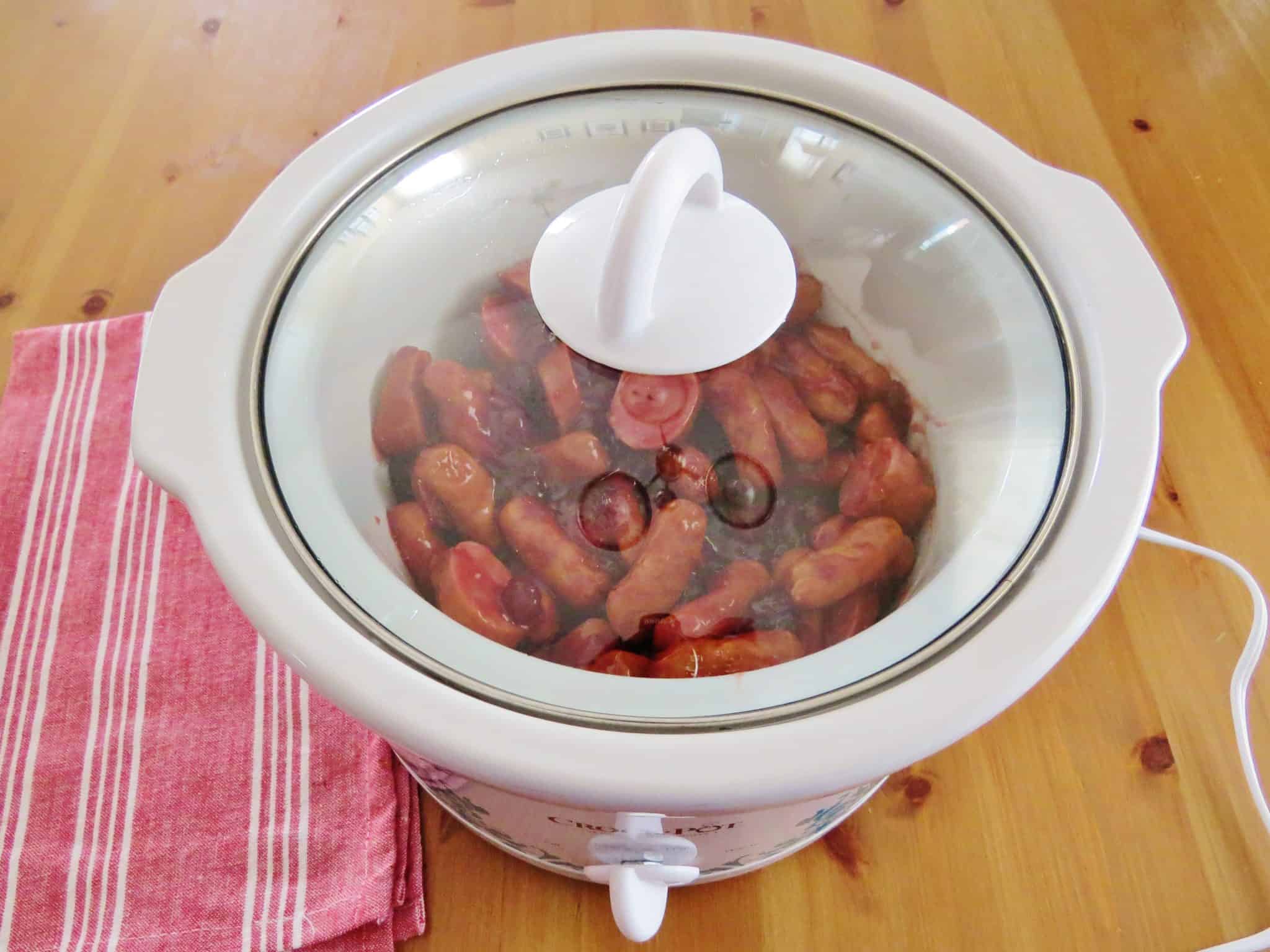 covered slow cooker with sausages cooking inside. 