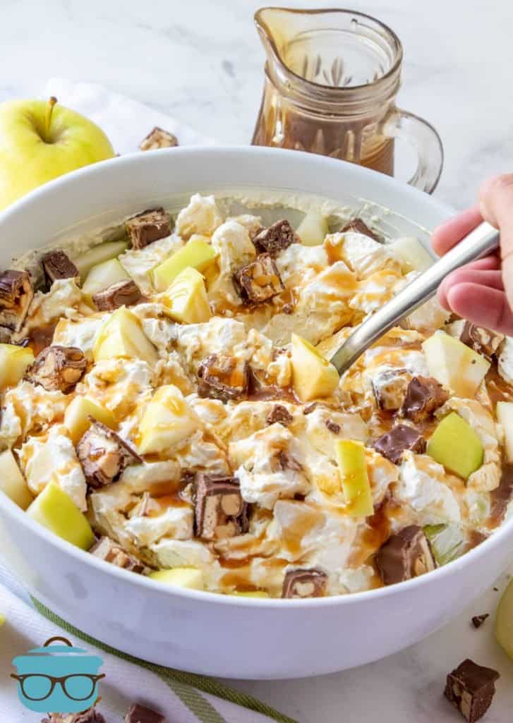 Snickers Caramel Apple Salad in a large white bowl with a spoon inserted