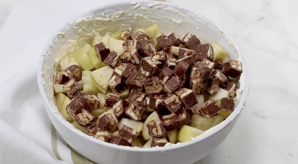 chopped apples and chopped snickers bars offed to cool whip mixture in a bowl