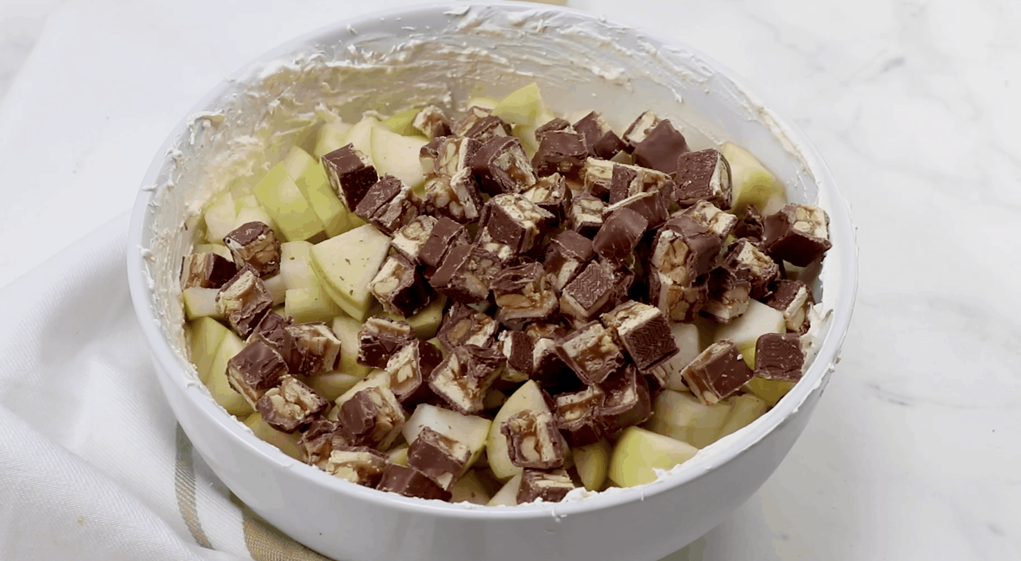 chopped apples and chopped snickers bars offed to cool whip mixture in a bowl.
