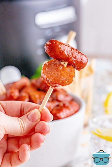 a hand holding up a toothpick holding up two glazed sausage bites.