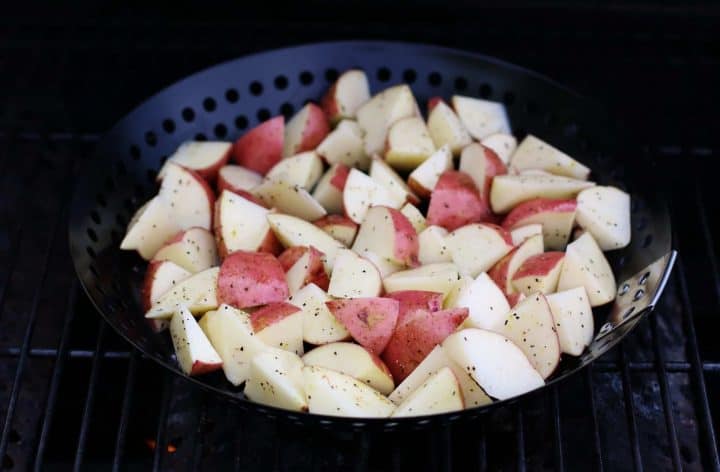 seasoned diced red potatoes in a grill pan shown on the grates of a gas grill.