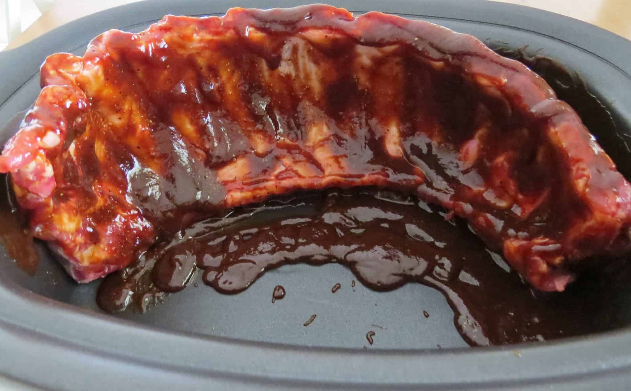 baby back ribs covered in barbecue sauce standing on its side in a slow cooker