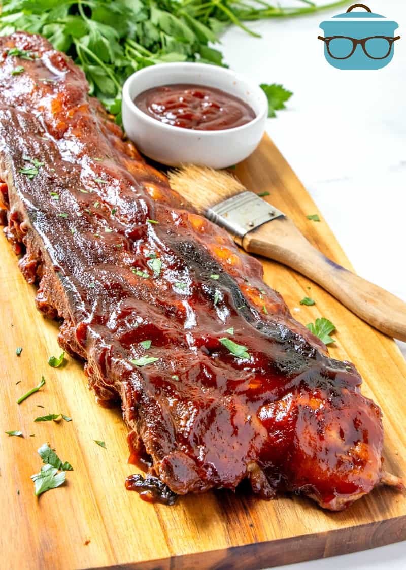 whole rack of cooked bbq ribs on a wooden platter and slathered in BBQ sauce.
