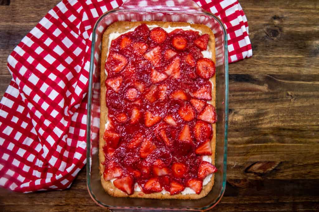 strawberry topping spread on top of sweet cream cheese mixture in a clear glass baking dish.