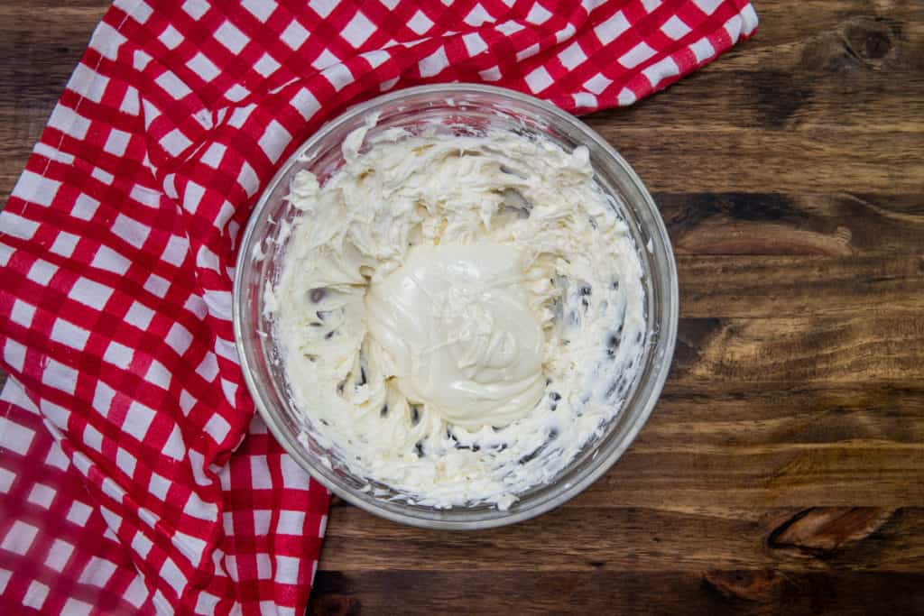 softened cream cheese mixed together with melted white chocolate chips in a glass bowl.